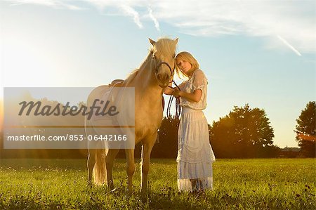 Lächelnde Frau in weißen Kleid mit Pferd auf der Wiese