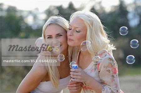 Two happy young blond women blowing soap bubbles outdoors