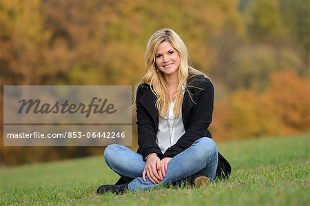 Smiling blond young woman sitting in autumnal meadow