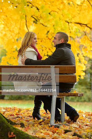Couple isitting on park bench n autumnal landscape