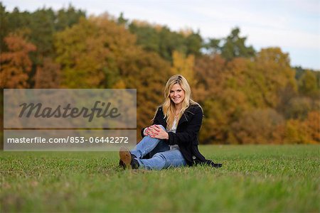 Blonde junge Frau in herbstlicher Wiese sitzt lächelnd
