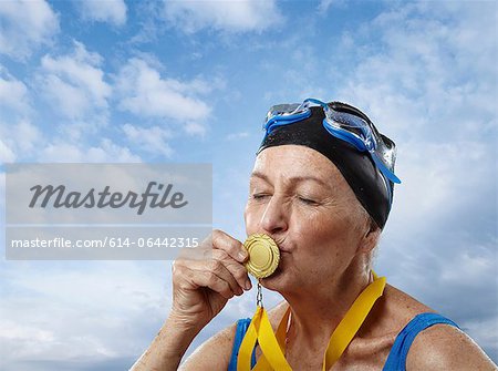 Senior woman wearing swimming cap kissing gold medal