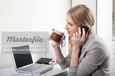 Young woman in office with cellphone and coffee