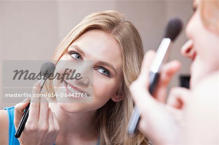 Young woman applying blusher in the mirror