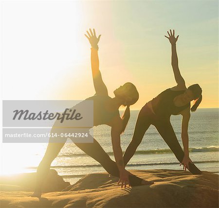 Two women practising yoga on beach in sunlight