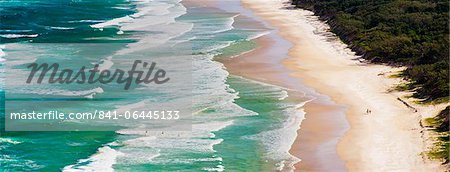 Panoramic photo of surfers heading out to surf on Tallow Beach at Cape Byron Bay, New South Wales, Australia, Pacific