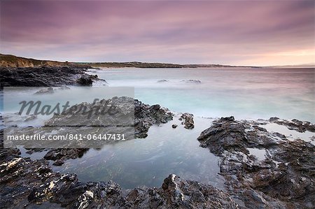 Looking over St Ives Bay towards Hayle from the rocky shores of Godrevy Point at sunset, Cornwall, England, United Kingdom, Europe