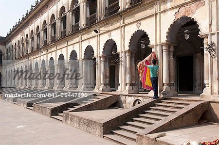 Man hanging out washed Quran cover cloths outside arched madrasa rooms in the Hugli Imambara, Hugli, West Bengal, India, Asia