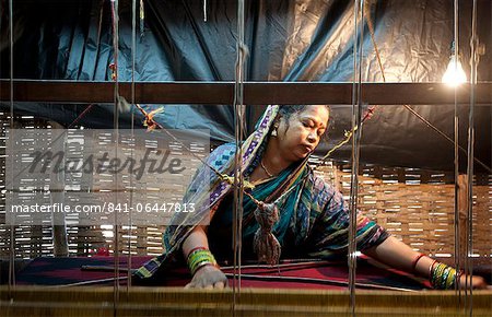 Woman in blue patterned sari weaving at loom in rough village shack, Naupatana weaving village, rural Orissa, India, Asia