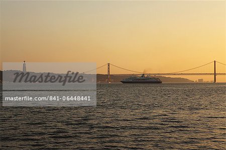 A cruise liner turns into the sunset, on the River Tagus under the 25 April Bridge and Christus Rei statue, Lisbon, Portugal, Europe