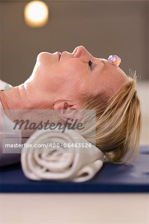 Senior woman relaxing and lying on pad with amethyst, quartz and other crystals on body. Side view