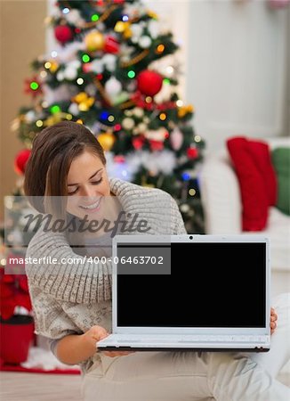 Happy woman looking laptop blank screen near Christmas tree