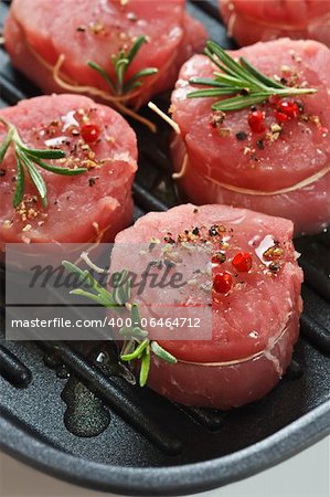 Fresh meat with spices and rosemary on a grill pan.
