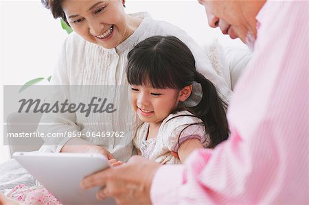 Grandparents and granddaughter using electronic tablet on the sofa