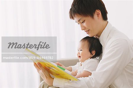 Father reading a baby book to his son on the sofa