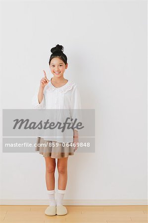 Girl in pre-adolescent age pointing a finger up in front of a white wall