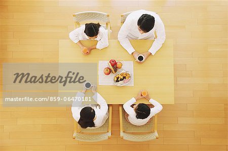 Family of four people drinking coffee and juice at the dining table seen from above