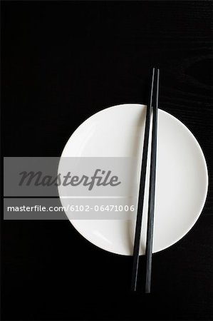 White plate with chopsticks on black background