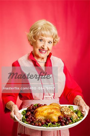 Sweet retro grandmother holding a Christmas or Thanksgiving holiday turkey dinner.  Red background.