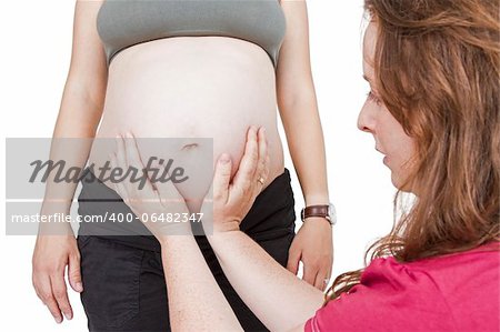 young midwife fingering at human belly. pregnant woman standing while midwife is sitting in front. horizontal picture isolated on white