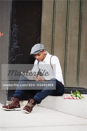 Portrait of Man Sitting on Step with Flowers, Using a Tablet, Mannheim, Baden-Wurttemberg, Germany