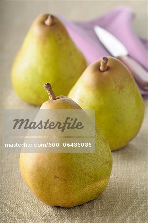 Close-up of Three Pears with Knife on Beige Background, Studio Shot