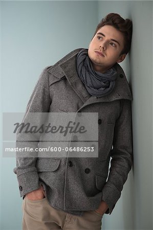 Portrait of Young Man wearing Grey Scarf and Jacket, Leaning against Wall, Studio Shot on Grey Background