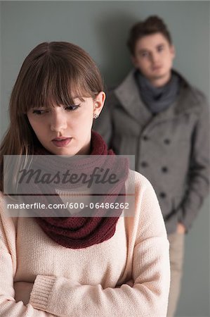 Portrait of Young Man Standing behind Young Woman, Looking at her Intensely, Studio Shot on Grey Background