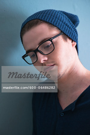 Close-up Portrait of Young Man wearing Woolen Hat and Horn-rimmed Eyeglasses, Looking Downward, Studio Shot on Blue Background