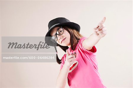 Portrait of Girl wearing Fedora and Horn-rimmed Eyeglasses, Pointing and Smiling at Camera, Studio Shot on White Background