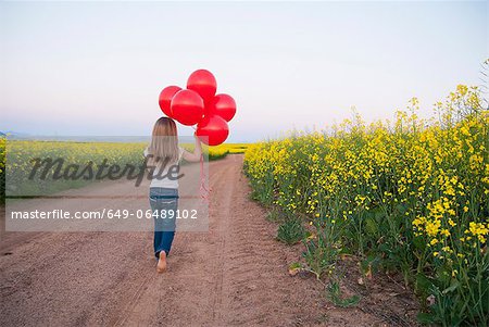 Girl carrying balloons on dirt road