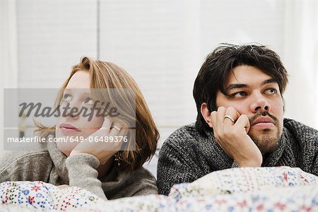 Couple resting chins in hands on bed