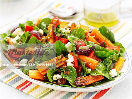 A colourful plate of salad with roasted carrots, dried tomatoes, red peppers, sheep's cheese, spinach, herbs and nuts