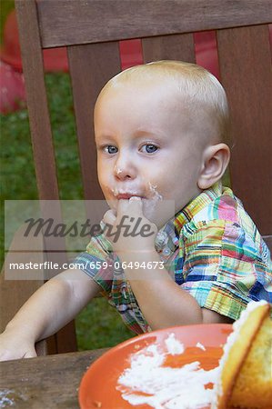 Little Boy Licking the Frosting Off His Fingers from a Cupcake; Sitting at an Outdoor Table