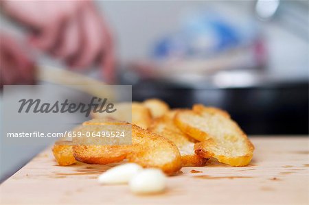 Toasted baguette slices being rubbed with garlic