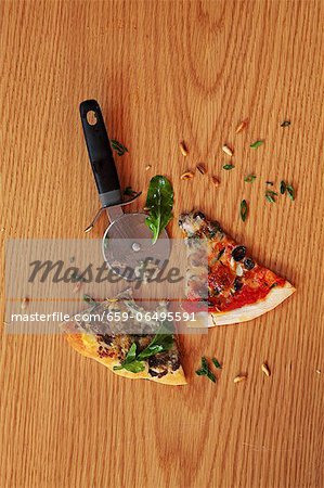 Slices of pizza and a pizza wheel on a wooden surface