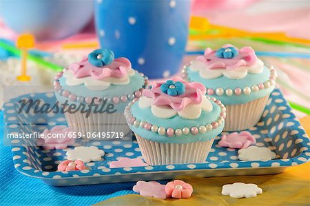 Light blue cupcakes decorated with pink flowers and sugar balls