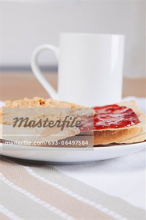 Peanut butter and jam on slices of bread with cup of coffee