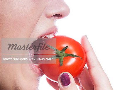 Detail shot of young woman eating tomato over white background