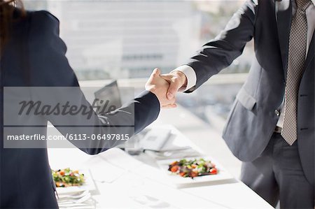 Businessman and businesswoman shaking hands at table with lunch