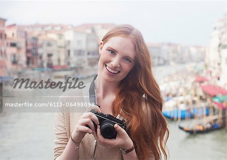 Portrait of smiling woman holding digital camera at waterfront in Venice