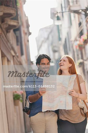 Smiling couple walking with map on narrow street in Venice