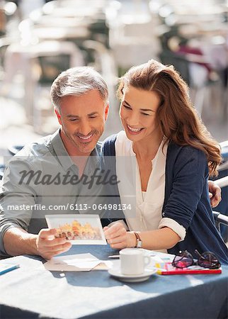 Smiling couple looking at postcard at sidewalk cafe