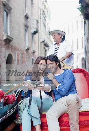 Smiling couple taking self-portrait with digital camera in gondola on canal in Venice