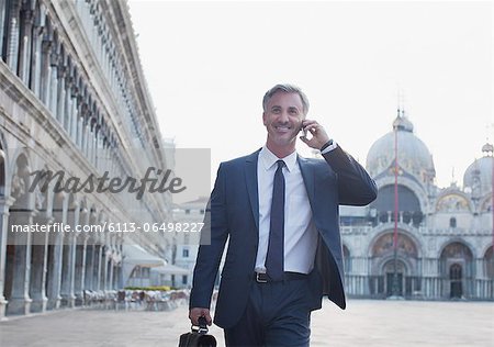 Smiling businessman talking on cell phone and walking through St. Mark's Square in Venice