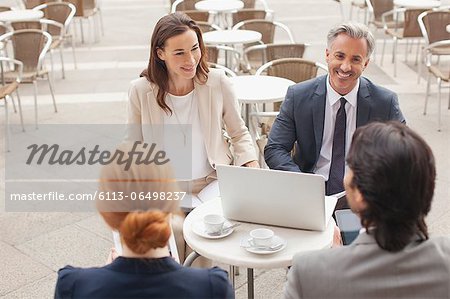 Smiling business people with laptop meeting at sidewalk cafe