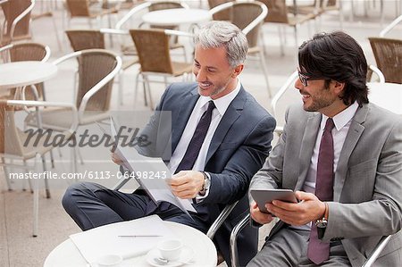 Smiling businessmen with digital tablet and paperwork in cafe