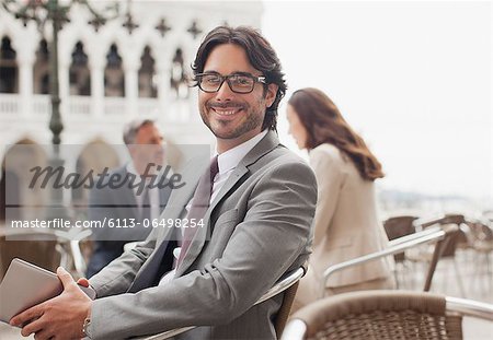 Portrait of smiling businessman holding digital tablet at sidewalk cafe in Venice