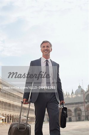 Smiling businessman pulling suitcase through Saint Mark's Square in Venice