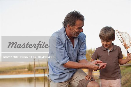 Smiling grandfather and grandson fishing at lakeside